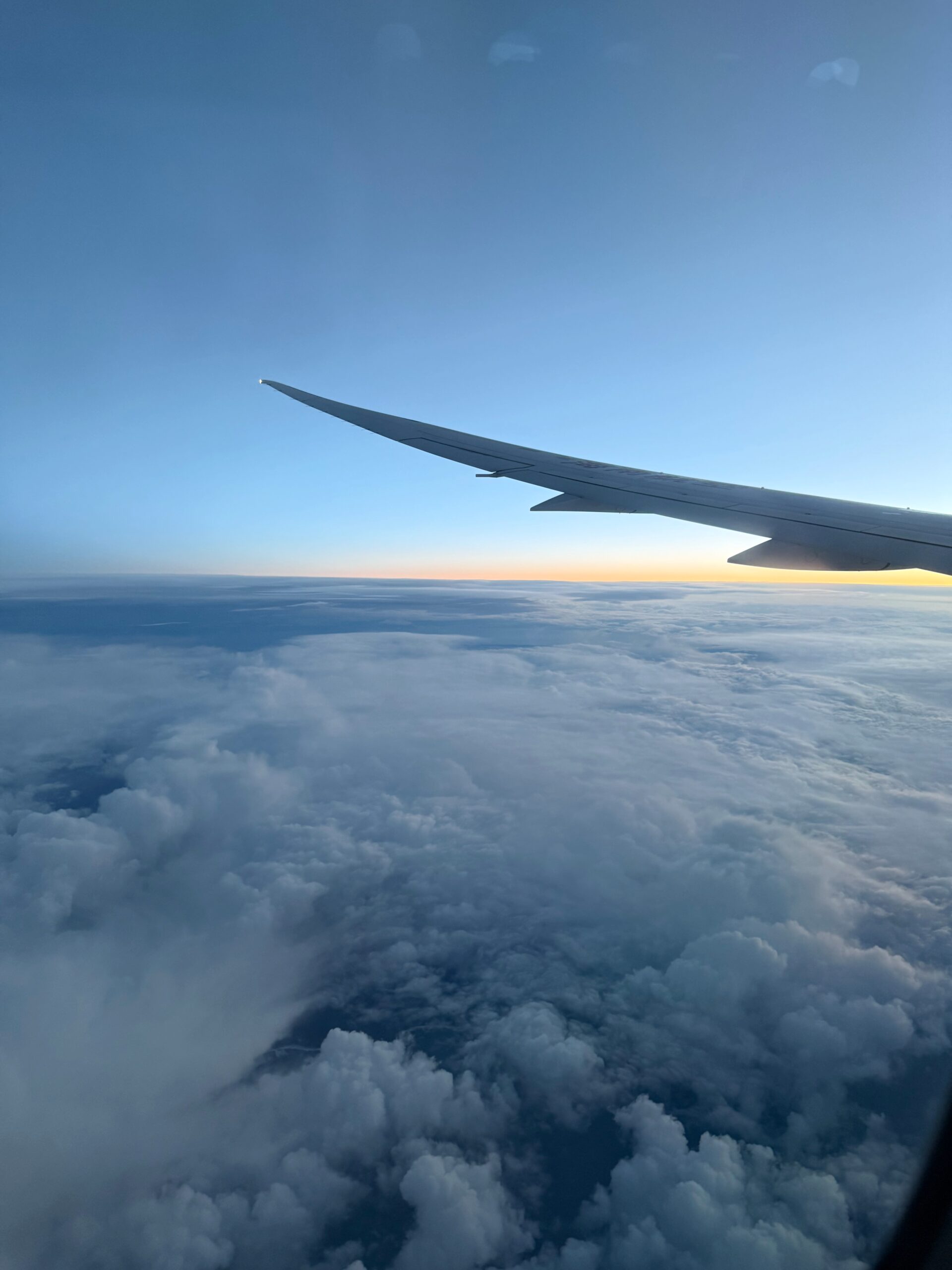 Airplane wing above clouds at sunrise, viewed from a window seat