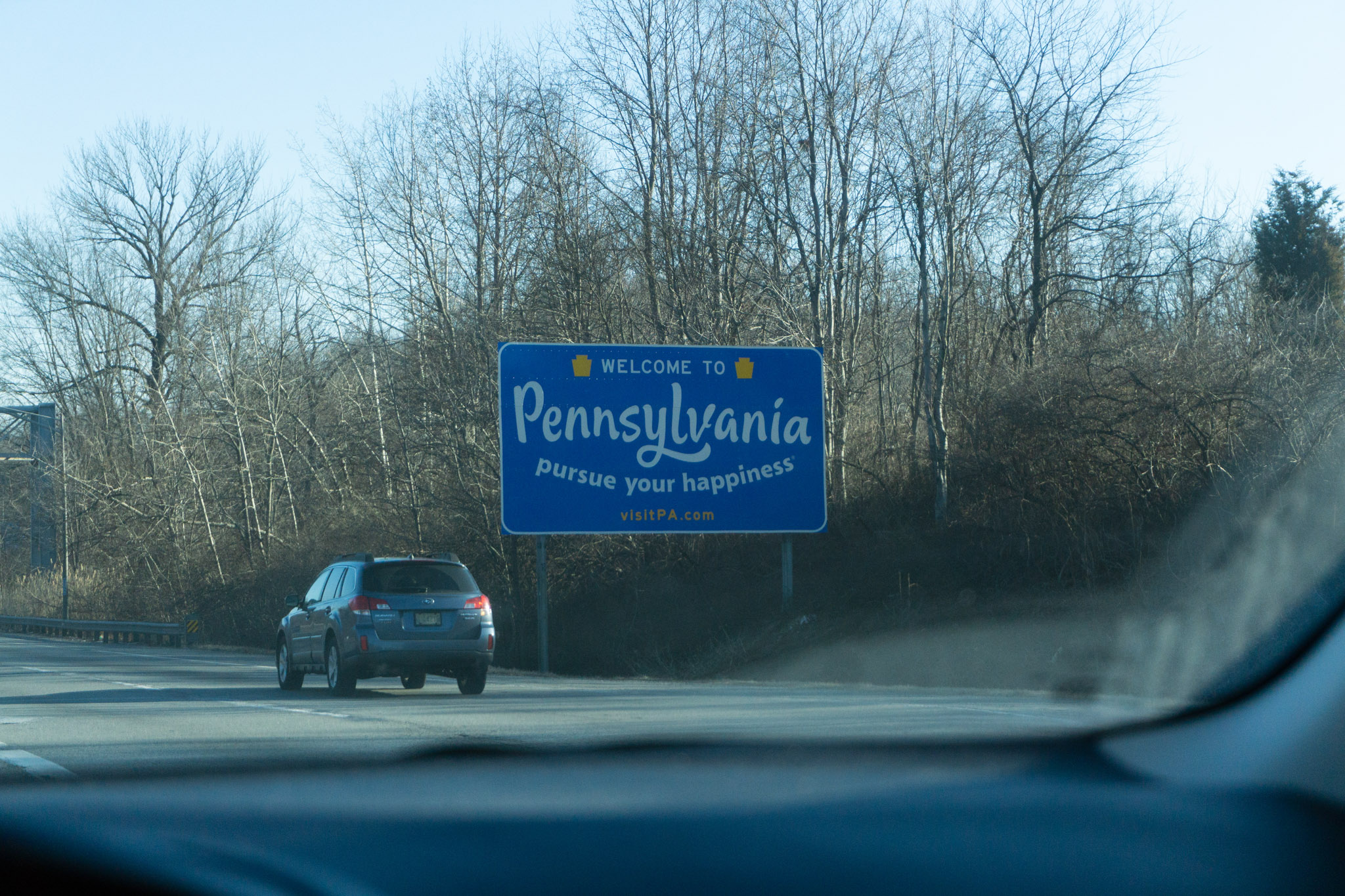 Blue Welcome to Pennsylvania Pursue Your Happiness road sign at the Delaware and PA state border.