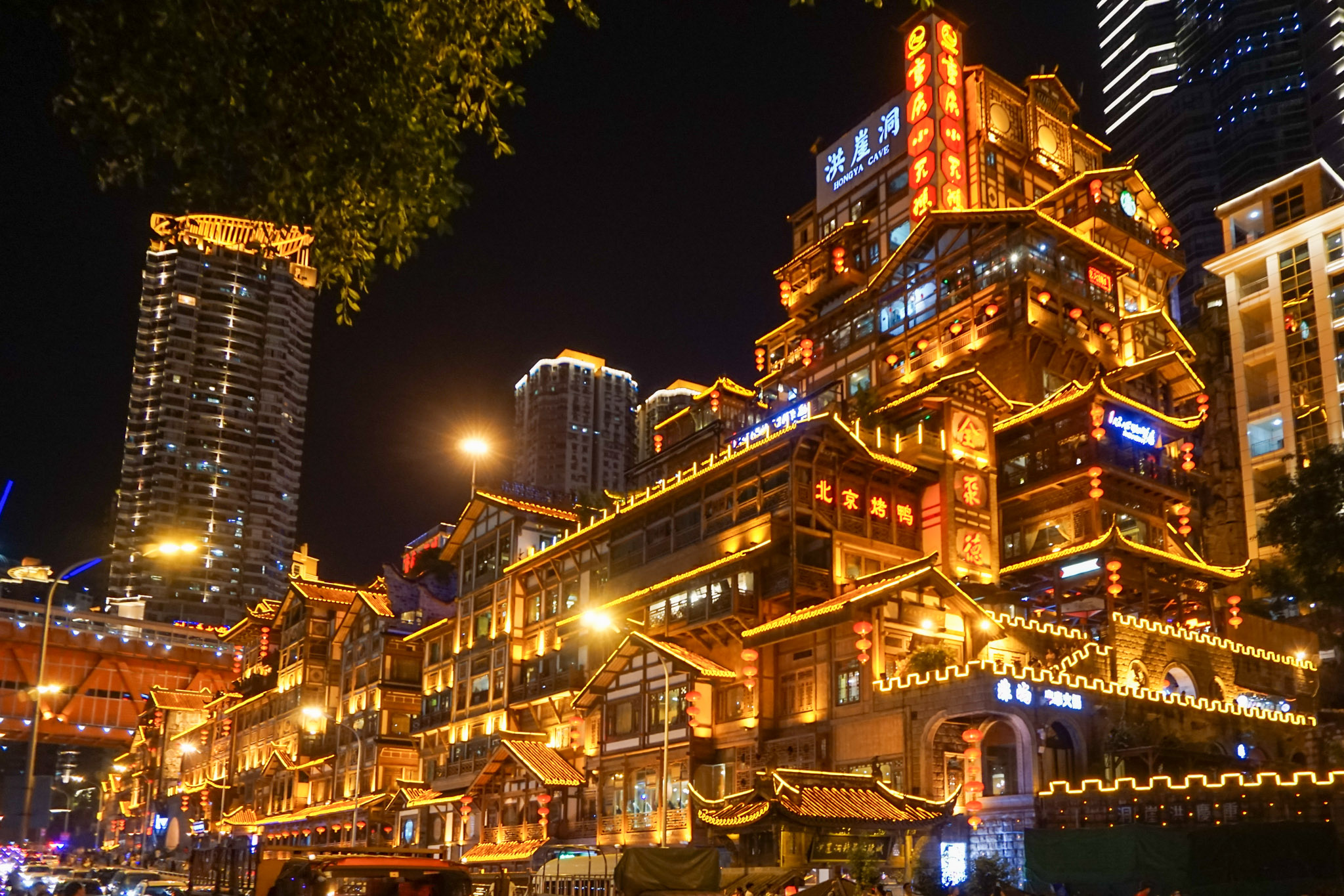 Night view of Hongyadong in Chongqing, with glowing traditional-style buildings, lantern lights, and a lively city street scene.